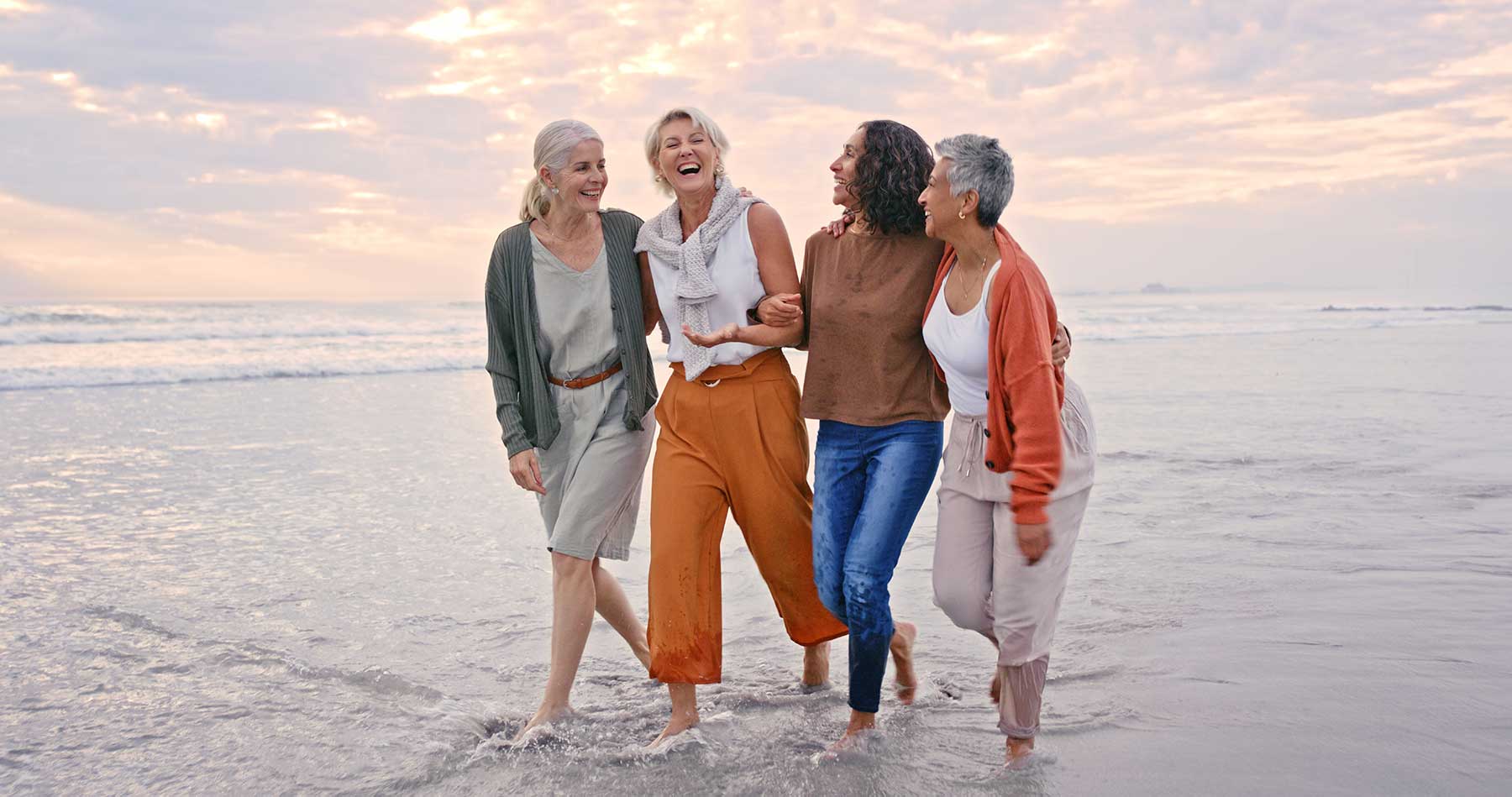 4 women walking on the beach laughing. 